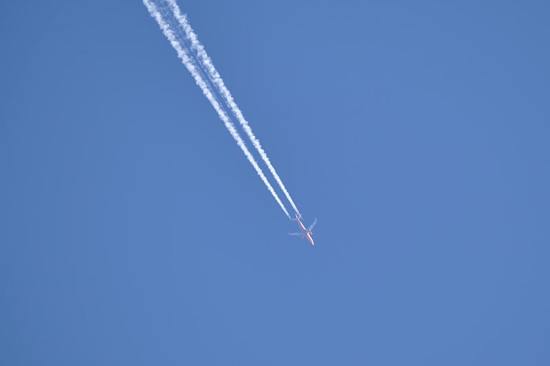 远处的喷气式客机在晴空万里的高空飞行，留下白色的烟雾和尾迹。航空运输的概念