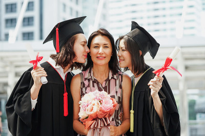 毕业日大学妇女和家庭，女孩拿着文凭和气球祝贺毕业日。