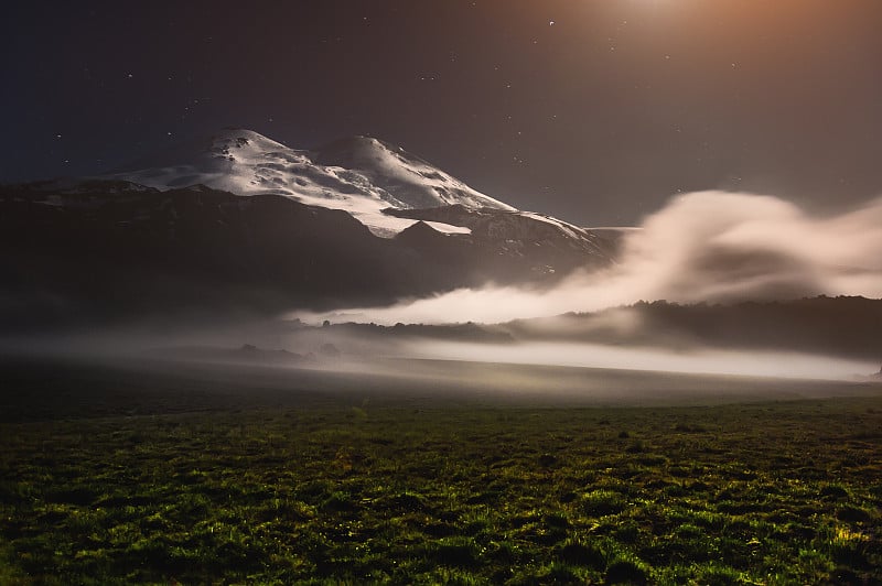 在夜晚的月光下，高加索地区沉睡的厄尔布鲁斯火山附近漂浮着一朵云