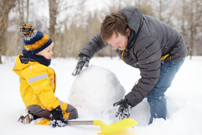 小男孩和他的父亲在下雪的公园堆雪人。冬季与孩子们一起进行户外活动。