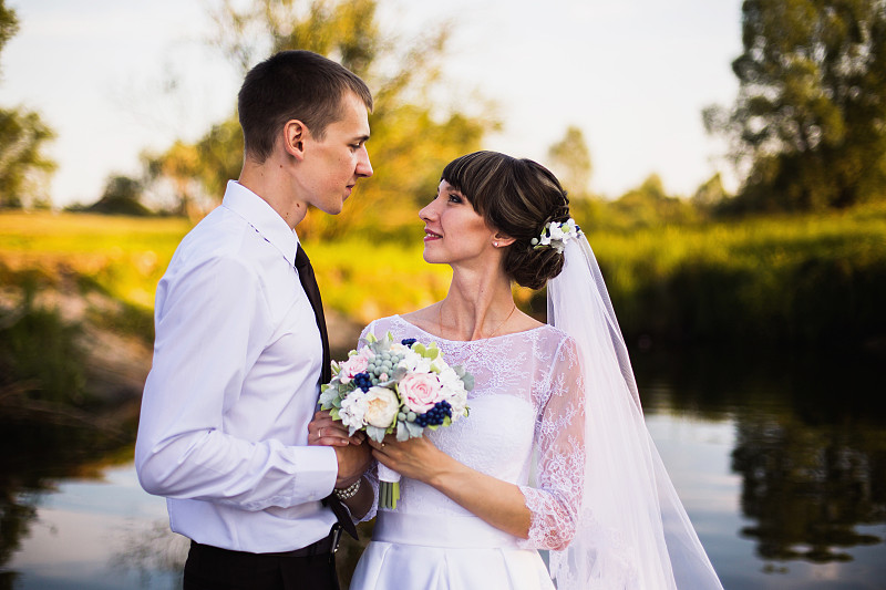 新婚夫妇在阳光下感受大自然。男人和女人之间的爱情。穿着婚纱的新娘。穿西装的新郎。美丽的婚礼花束。夏天