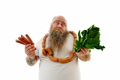 一位脖子上绕着香肠的体重超标男子在选择食物时遇到了困难:香肠还是菠菜。肖像孤立在白色背景