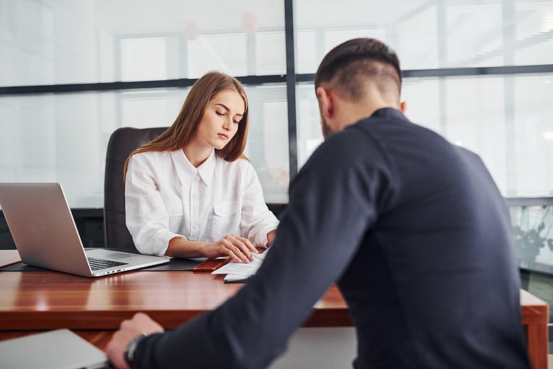 拿着文件坐着的家伙。女人和男人穿着正式的衣服一起在室内的办公室靠桌子工作