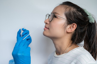 医生试图从亚洲女性身上提取鼻拭子，以检测covid-19感染的诊断。
