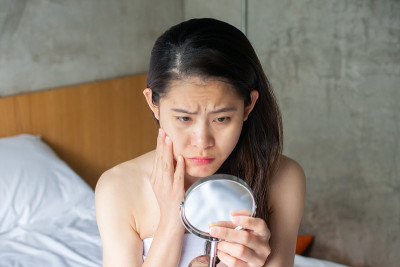 肖像亚洲妇女担心她的脸时，她看到了问题的痤疮和疤痕的迷你镜。