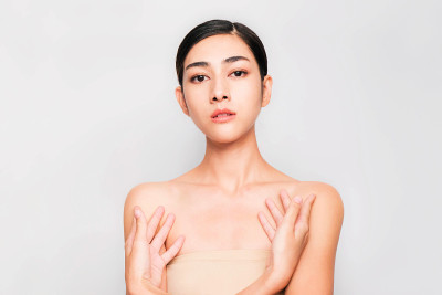 年轻美丽的亚洲女人与干净和明亮的皮肤，化妆品美丽的概念，手触摸脸颊，微笑和友好的脸孤立在灰色的背景