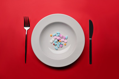 补品作为食物放在白色的圆形盘子上，配以刀叉。用维生素代替食物的概念。