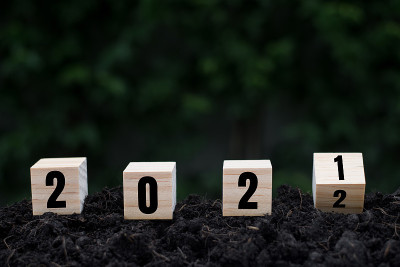 手翻转的木制立方体块的土壤和绿色叶子自然背景变化的2021年到2022年。新年和节日概念。
