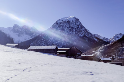 太阳耀斑在积雪覆盖的山坡和小木屋上。