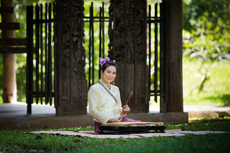 亚洲女士与微笑在泰国传统想要打扮坐和演奏扬琴