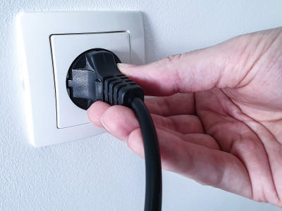 用一只手在白色塑料电源插座内断开黑色电源插头