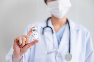 一名戴着口罩的女医生站在实验室里，手里拿着一瓶保护冠状病毒的疫苗。预防COVID-19传播的概念。