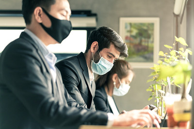新常态的生活方式概念，商务人士戴着面具坐着，保持社交距离，在公共区域工作，或与笔记本电脑和智能手机共