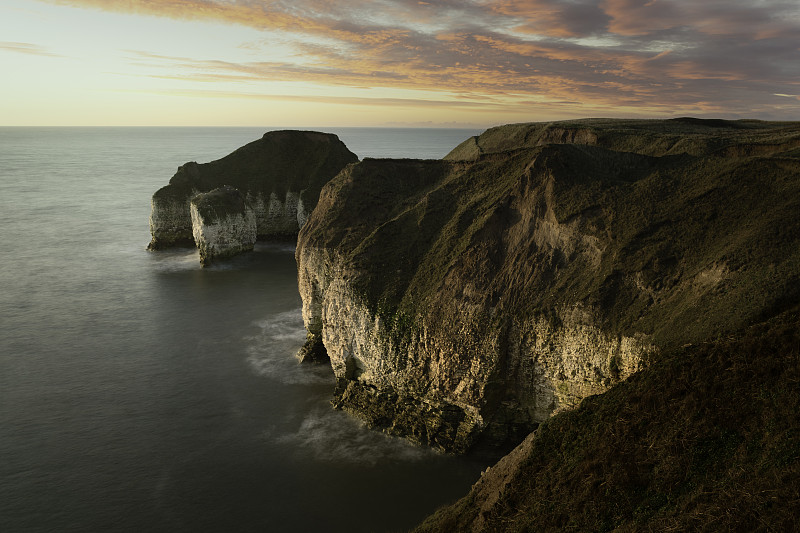 海面上的日出和海岸线上明亮的天空下被侵蚀的白垩峭壁。Flamborough,英国。