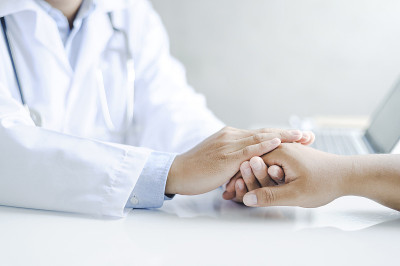友好的男医生手牵着病人的手，坐在桌旁鼓励、同情、鼓励和支持。坏消息减少，医药和保健观念