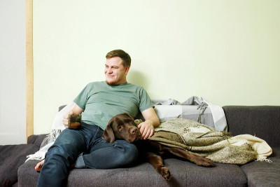 帅哥坐在家里的沙发上和宠物狗拉布拉多寻回犬在一起