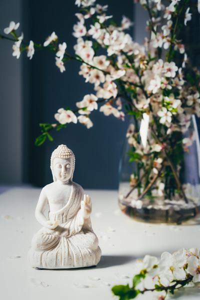 黑色背景的花瓶上装饰着白色的佛像和开花的树枝。冥想和放松仪式。佛陀的生日。垂直的名片。有选择性的重点