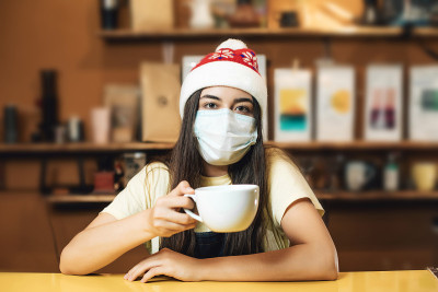 女服务员和咖啡师的新年肖像与保护面部面具室内咖啡馆。冠状病毒概念后的新常态。戴着圣诞红帽子的女孩