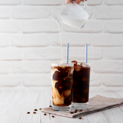 高脚杯冰咖啡拿铁卡布奇诺，奶油或牛奶倒在andÂ coffeeÂ咖啡豆和吸管上，灯光背景。清凉可口的