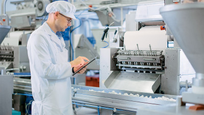 年轻男性质量主管或食品技术员正在检查饺子工厂的自动化生产。7 .员工使用平板电脑工作。他戴着白色卫生