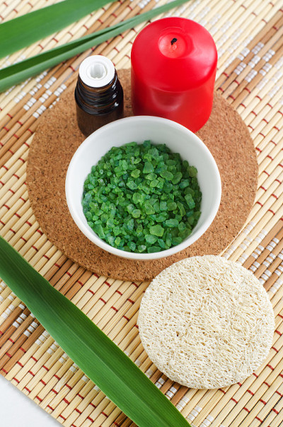 白色的小碗里放着绿色芳香浴盐(泡脚)，红蜡烛，丝瓜海绵和绿叶。芳香疗法，水疗和草药概念。