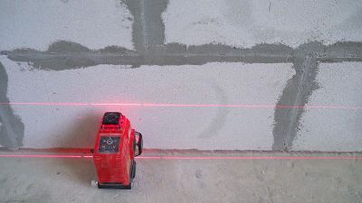建筑工在建筑工地用激光水平仪进行安排。建筑激光水平仪和墙壁表面标记的红线。激光水平对砌块墙