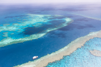 鸟瞰海峡与水肺潜水旅游船通过大堡礁附近的airlie海滩被浅水珊瑚礁包围在蓝绿色的清澈的水。