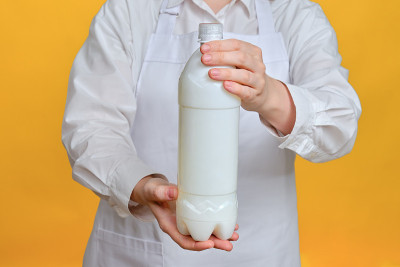 黄色背景下的男厨师手里拿着一瓶塑料牛奶