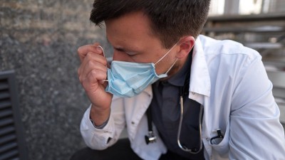 严肃的医生在医院上了很长时间班后正在楼梯上休息。疲惫的医生戴着口罩，白色制服和听诊器坐在诊所外面的楼