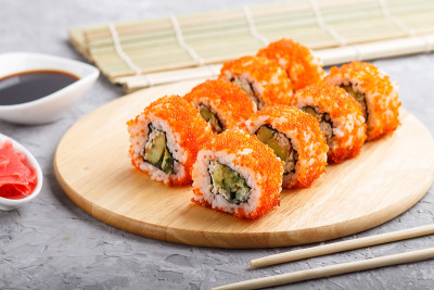 日本寿司卷与飞鱼卵，筷子，酱油和腌制生姜在木板上，在灰色的混凝土背景。侧视图，特写，选择性聚焦。