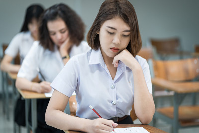 选择性焦点的青少年大学生坐在讲座椅上做期末考试和写在试卷上的答题卡在教室里。大学生在教室里穿制服。