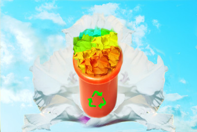 有回收标志的垃圾桶里装满了五颜六色的废纸。剑兰和蓝天的背景。循环利用、自然环保的理念。