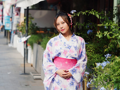 迷人的亚洲女人的肖像穿着传统的日本和服，微笑和摆姿势在阳光明媚的春天街道与手在腰部，真实的人的生活方