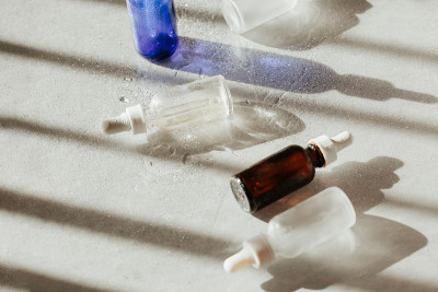白色和蓝色的面部精华和面部油瓶与滴管在白色反光头发与水和光影。
