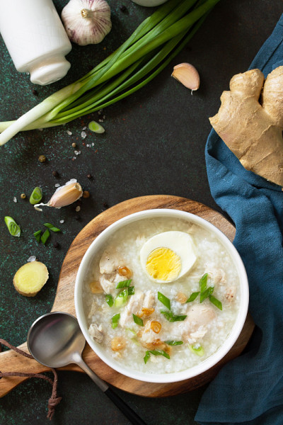 吃Arroz Caldo汤。姜、鸡、饭和大蒜的热汤，放在黑暗的工作台上。俯视图平铺背景。