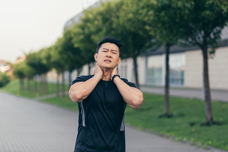 亚洲男运动员，上班前在公园里背着背包跑步，在公园体育场附近跑步时脖子酸痛得厉害