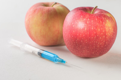 转基因和垃圾食品的概念。苹果和医用注射器与化学制剂在白色的背景