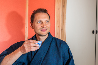 传统的日本房子客栈与年轻人快乐的脸拿着杯在和服在红壁龛喝绿茶