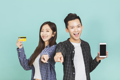 幸福的亚洲年轻夫妇显示手机和信用卡