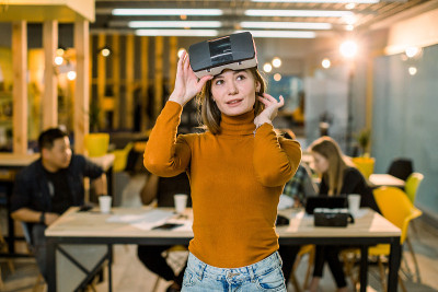 穿着橙色毛衣的漂亮女商务女性在工作中尝试3d vr眼镜。跨种族的年轻人团队在创意办公室一起工作