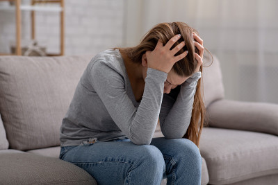 一个不幸的年轻女人双手抱头坐在沙发上，哭着，感觉很沮丧