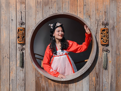 快乐的亚洲妇女游客穿着红色的汉服，古老的中国民族服装，看着窗外