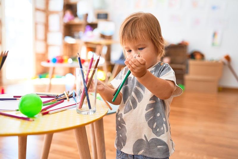可爱的幼童拿着铅笔在幼儿园里到处玩玩具