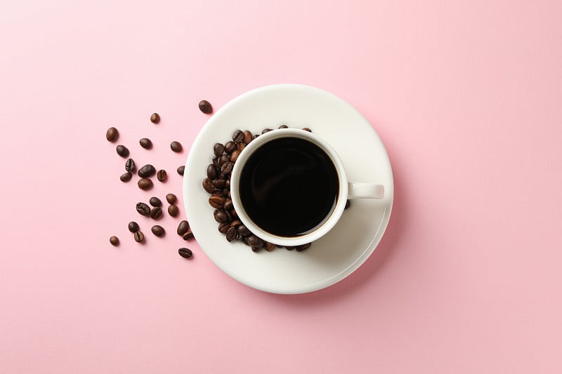 Cup of coffee and beans on pink background