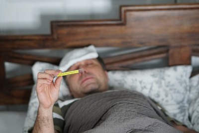 一个又累又病的男人躺在床上检查他的体温