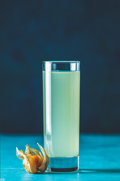 鸡尾酒与希腊茴香白兰地在高球玻璃，装饰的酸浆和红糖在蓝色的混凝土表面