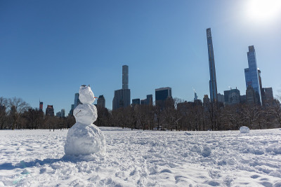 冬天在纽约中央公园的绵羊草地上的雪人，背景是曼哈顿中城的天际线