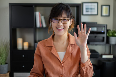 一名亚洲女性在视频通话中微笑着打招呼。积极情绪。