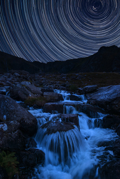 北极星周围的星迹数字合成图像和斯诺登尼亚的Llyn Ogwen和Llyn Idwal附近的山脉河流流