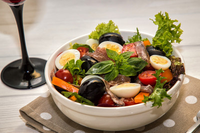近,宏。配红酒的法式晚餐。传统的niçoise(尼斯)沙拉在白色盘子上的圆点餐巾。